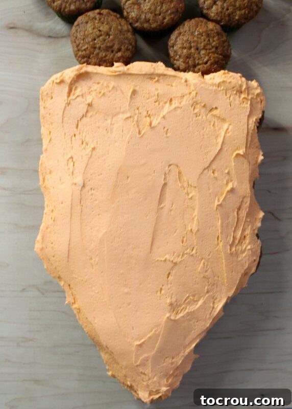 Pull-Apart Carrot Cake: A Cupcake Masterpiece 5 The orange frosting has been expertly smoothed over the carrot-shaped arrangement of cupcakes, creating a seamless and vibrant body for the pull-apart cake. The surface is even and perfectly shaped.