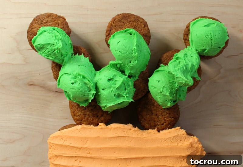 Pull-Apart Carrot Cake: A Cupcake Masterpiece 7 Scoops of vibrant green frosting have been carefully placed on the top section of the carrot cupcake cake, designated for the fronds. The placement includes filling the small gap between the main carrot body and the initial green cupcakes to ensure a seamless transition.