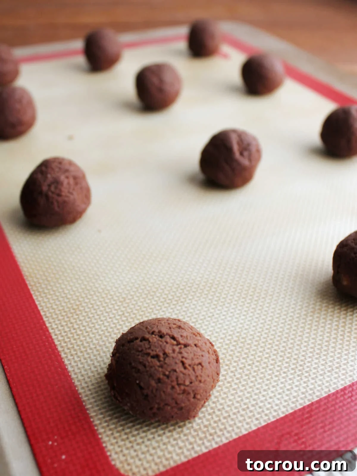 Fudgy Paw Print Double Chocolate Cookies 5 Balls of chocolate cookie dough on a cookie sheet that has a silicone mat on it.