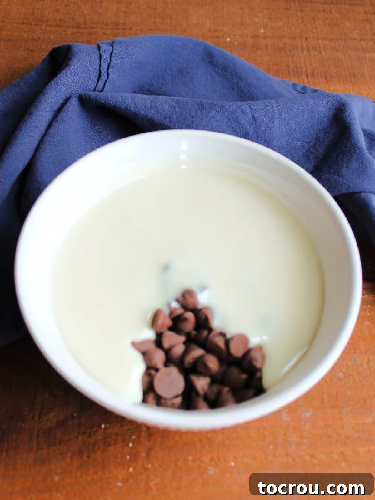 Chocolate Icing Ingredients A bowl containing a harmonious blend of sweetened condensed milk and glistening chocolate chips, poised to be melted down into a rich and smooth chocolate icing for the eclair cake.