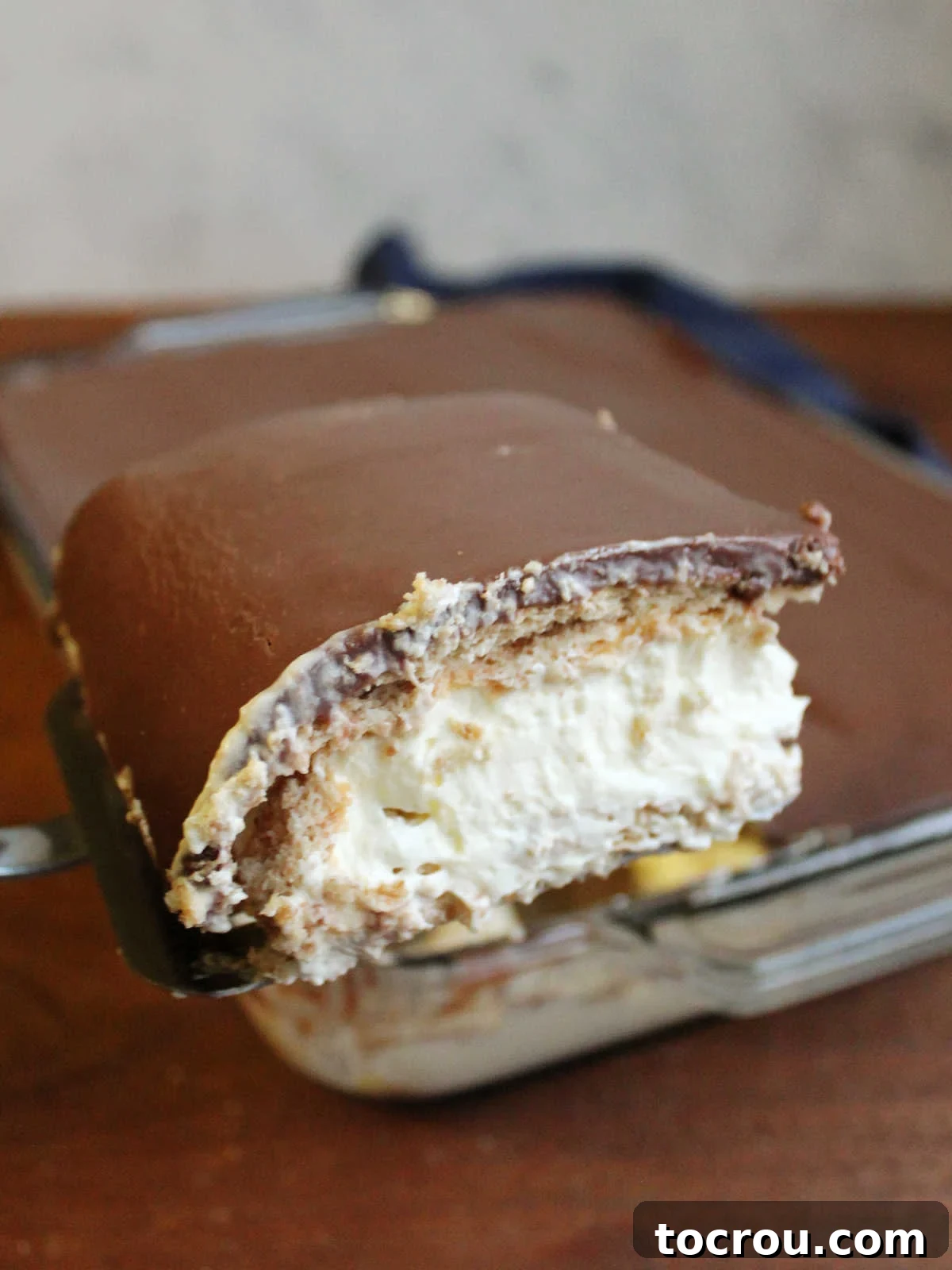 First Slice of Eclair Cake A spatula carefully lifts out the very first slice of a perfectly set eclair cake, showcasing its beautiful layers: crispy graham crackers transformed, a fluffy vanilla pudding mixture, and a glossy, fudgy chocolate icing crowning the top.