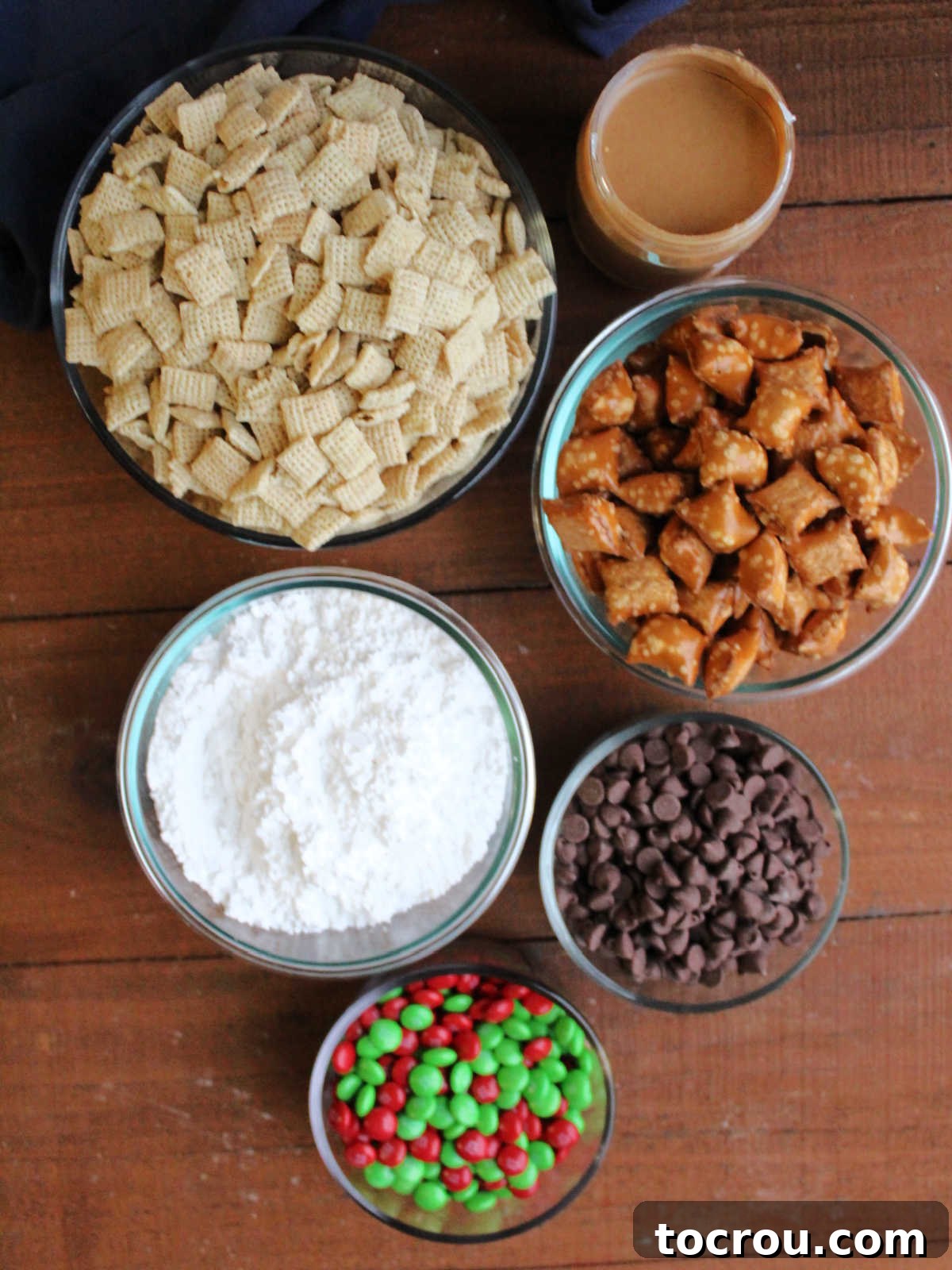 Ingredients including Chex cereal, peanut butter, peanut butter filled pretzels, chocolate chips, holiday M&Ms and powdered sugar.