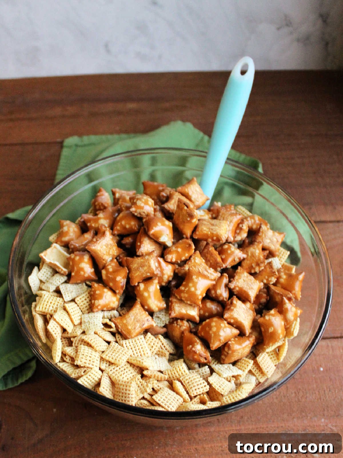 Adding corn and rice Chex cereal and some of the peanut butter filled pretzels into the bowl with the melted chocolate mixture.