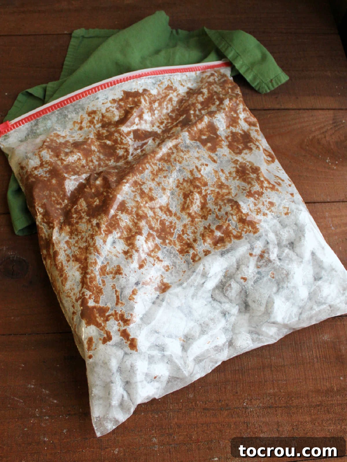 Large plastic bag with chocolate coated cereal mixture and powdered sugar inside after it has been shook to coat everything in the powdered sugar. 