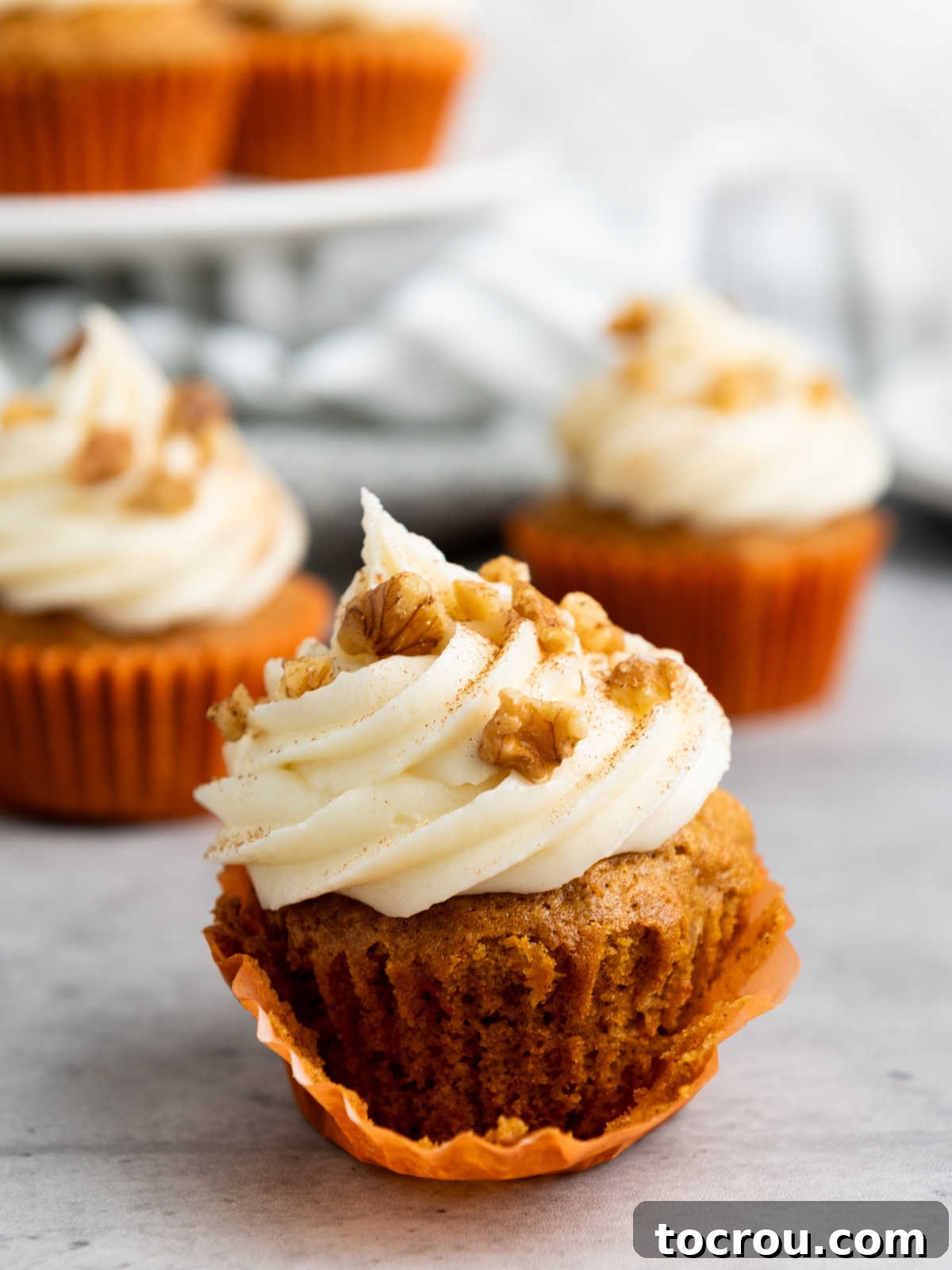 Rustic Carrot Cake Cupcakes 10 Taking wrapper off carrot cupcake showing the texture of the cake and fluffy frosting on top.