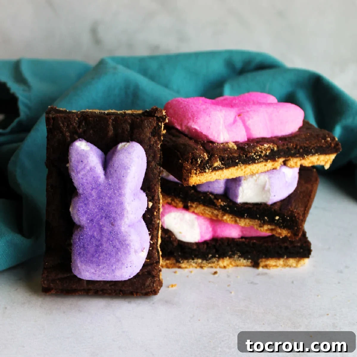 Super cute and really tasty s'mores bars can be yours in almost no time at all. They only require 5 ingredients and almost no effort! Stack of Peeps s'mores bars showing graham cracker base, gooey brownie-like chocolate layer and melted bunny shaped peeps on top, ready to be enjoyed.