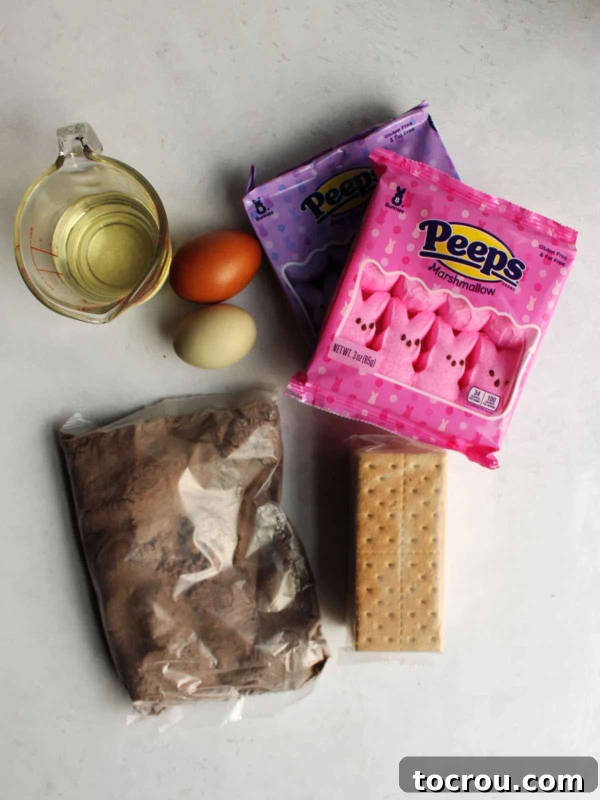 All the simple ingredients for Peeps S'mores bars laid out. Ingredients including chocolate cake mix, eggs, oil, graham crackers and peeps ready to be made into smores bars.