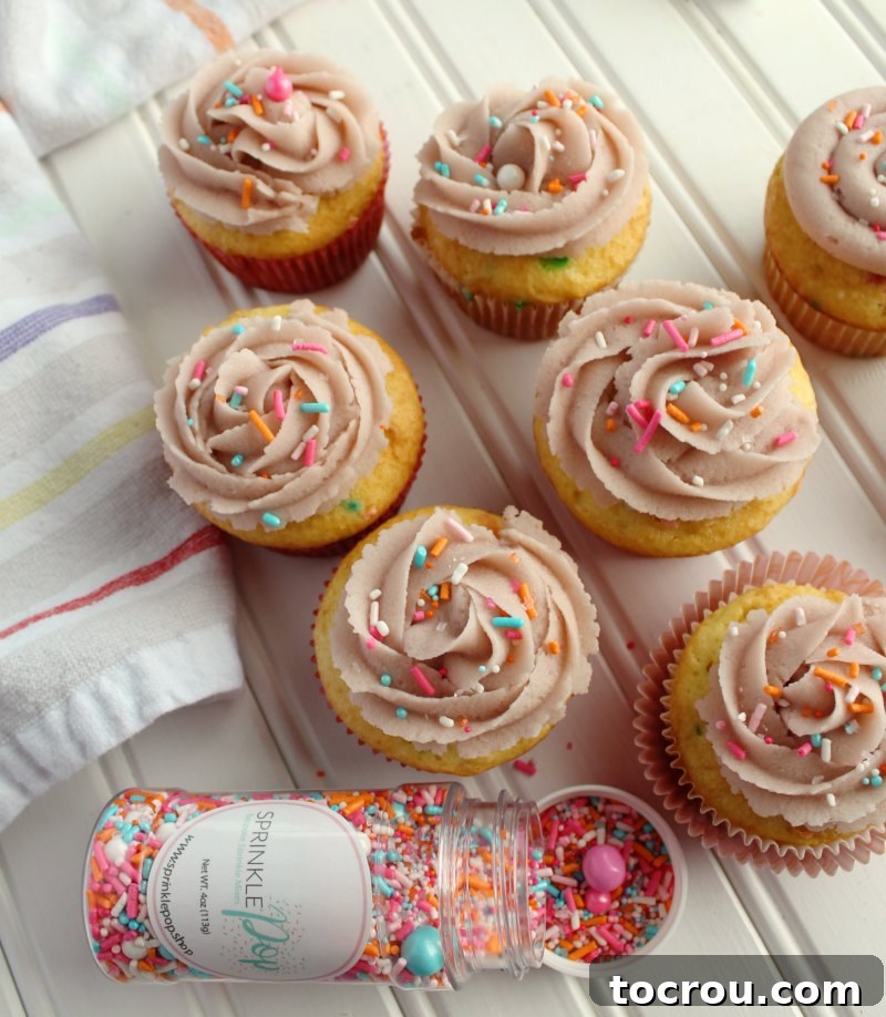 Sugar Cookie Dough Frosting Swirls on Cupcakes cupcakes with swirls of sugar cookie dough frosting and a bottle of springy sprinkles.