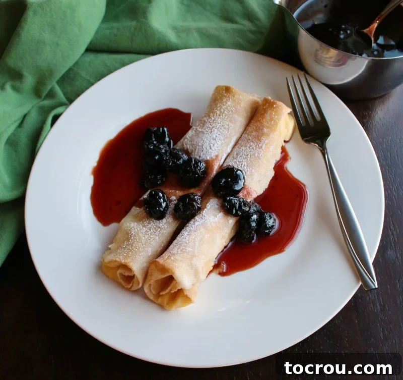 Two baked lemon ricotta stuffed crepes topped with powdered sugar and cherry sauce.