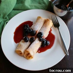 Two baked lemon ricotta stuffed crepes topped with powdered sugar and cherry sauce.