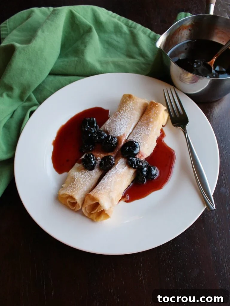 lemon ricotta stuffed crepes on plate with cherry syrup.