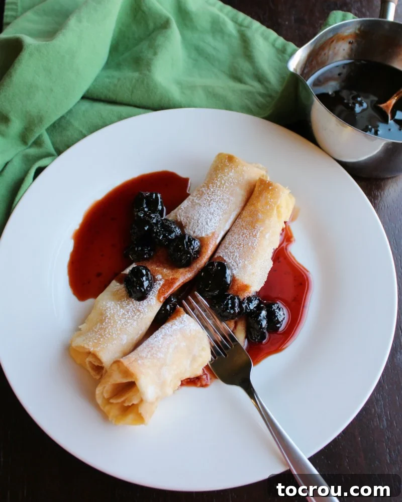 fork cutting into stuffed crepe covered with cherry syrup. pan of syrup in background.