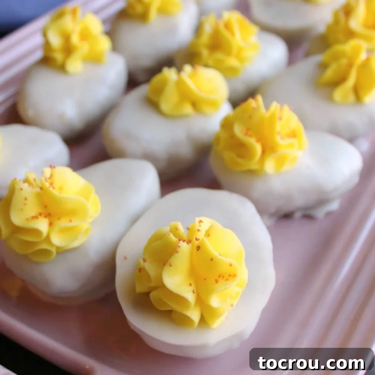 Platter of cake balls decorated to look like deviled eggs with white chocolate coating, yellow buttercream and a tiny sprinkle of red sanding sugar.