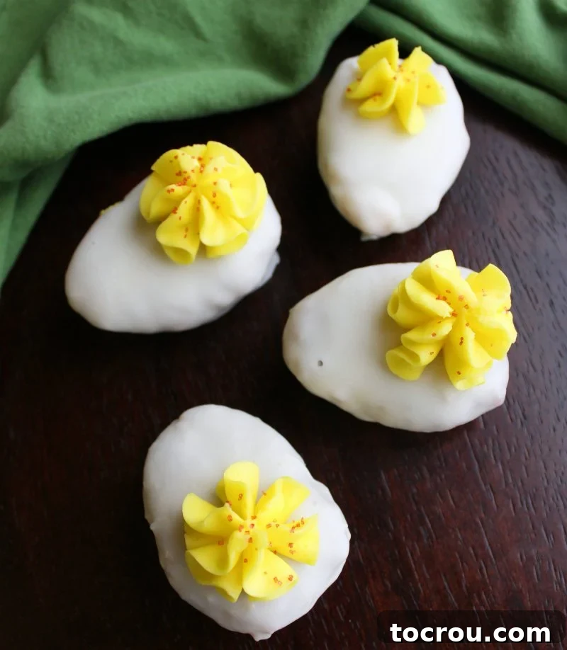 Four deviled egg cake balls dipped in white chocolate with yellow buttercream and red sugar to look like the yolk and paprika.