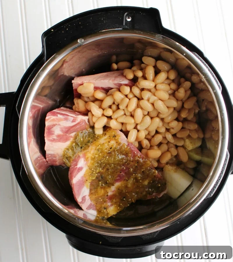 Zesty Instant Pot Salsa Verde Pork 3 Chunks of pork, sliced onions, creamy beans, and vibrant salsa verde neatly arranged in an Instant Pot, ready for pressure cooking.