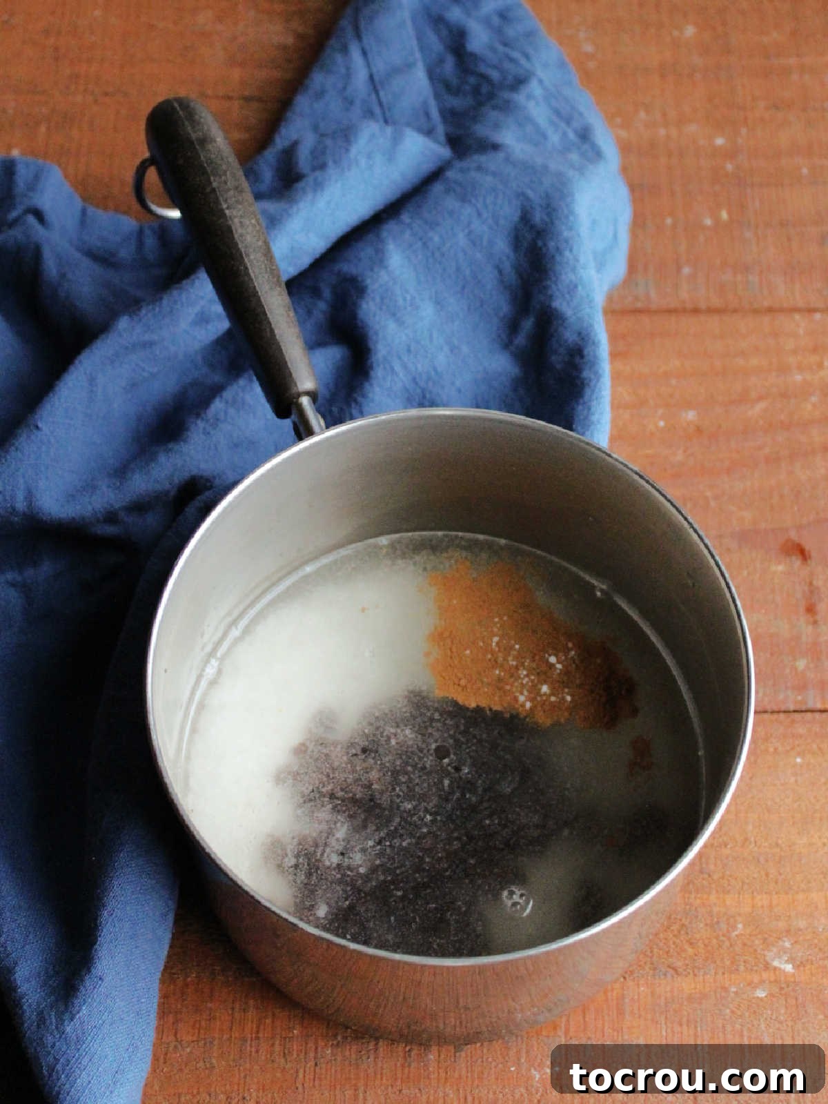 Long-grain rice, raisins, cinnamon, and salt soaking in a saucepan filled with water, preparing for cooking.