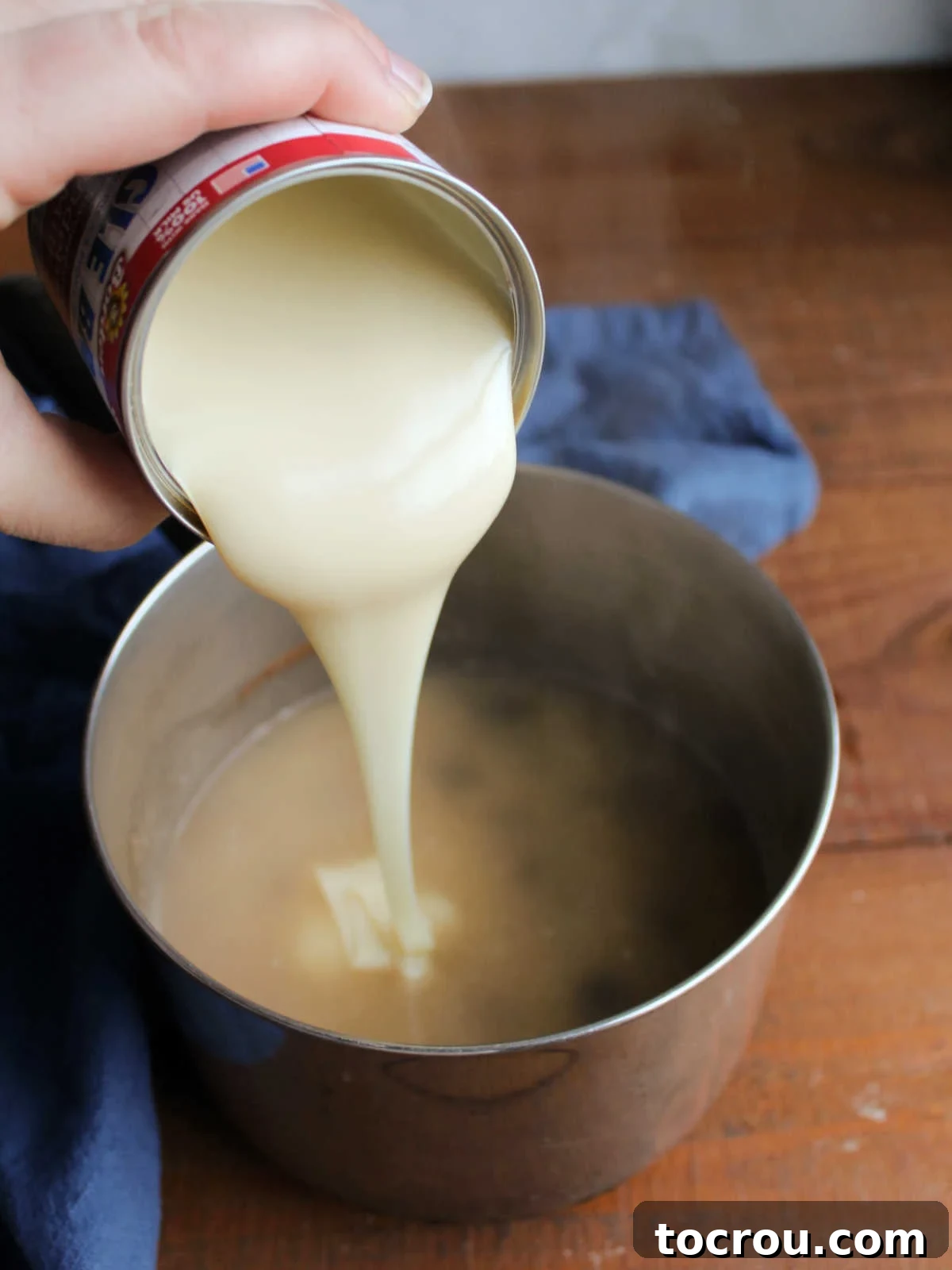 Pouring a can of rich sweetened condensed milk into the saucepan with the rice mixture after the water has come to a boil, preparing for further cooking.