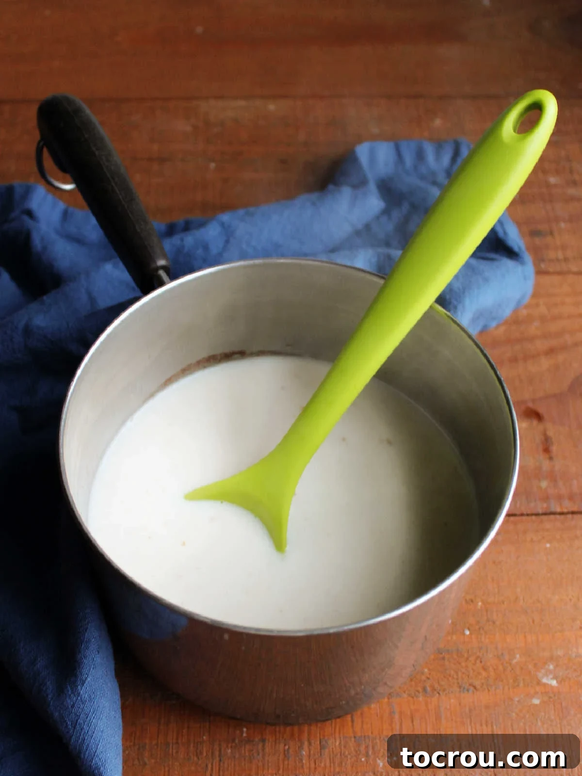 A saucepan containing the creamy rice pudding mixture, after the sweetened condensed milk has been thoroughly stirred in, ready to be brought back to a gentle boil.