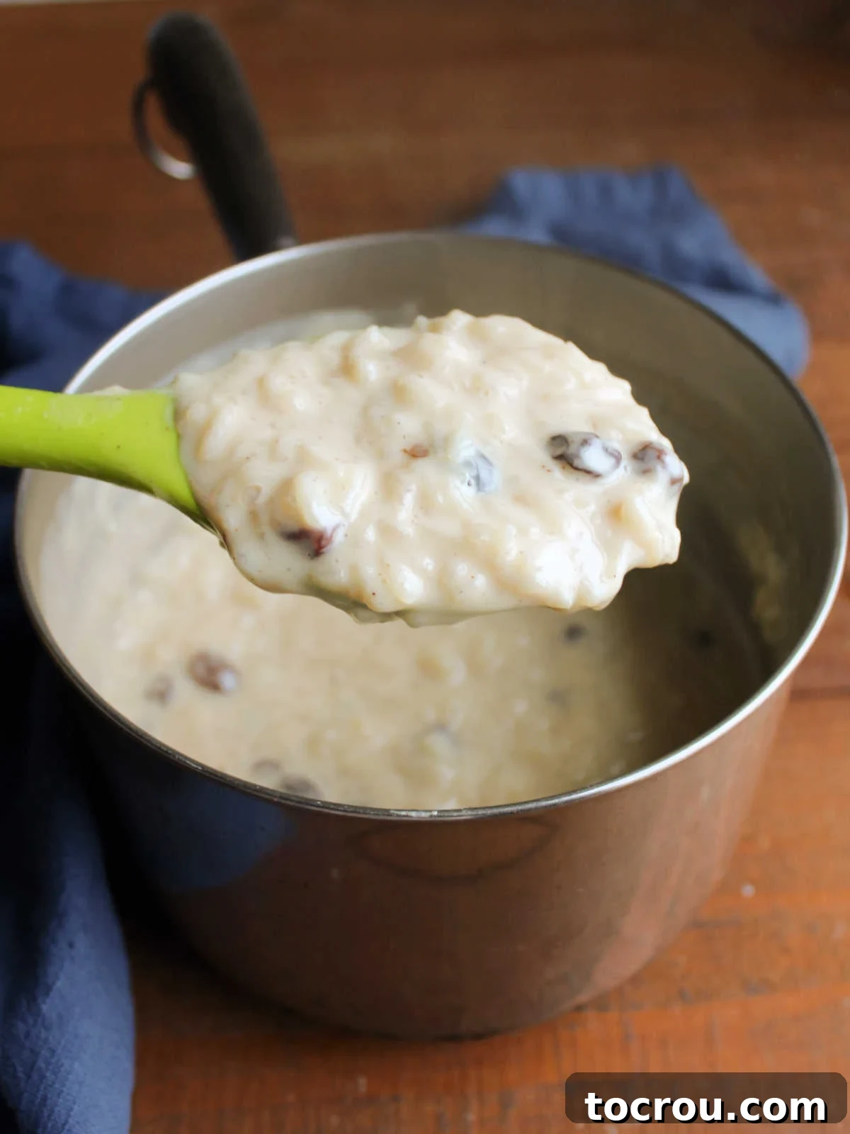 A spoon lifting a portion of thickened, creamy condensed milk rice pudding from the saucepan after it has been allowed to cool slightly, showing its ideal texture.