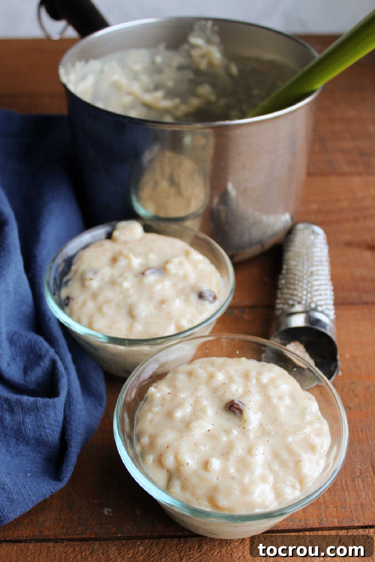 Two individual servings of creamy condensed milk rice pudding, garnished with a sprinkle of cinnamon, served in small glass bowls in front of the saucepan containing the remaining pudding.