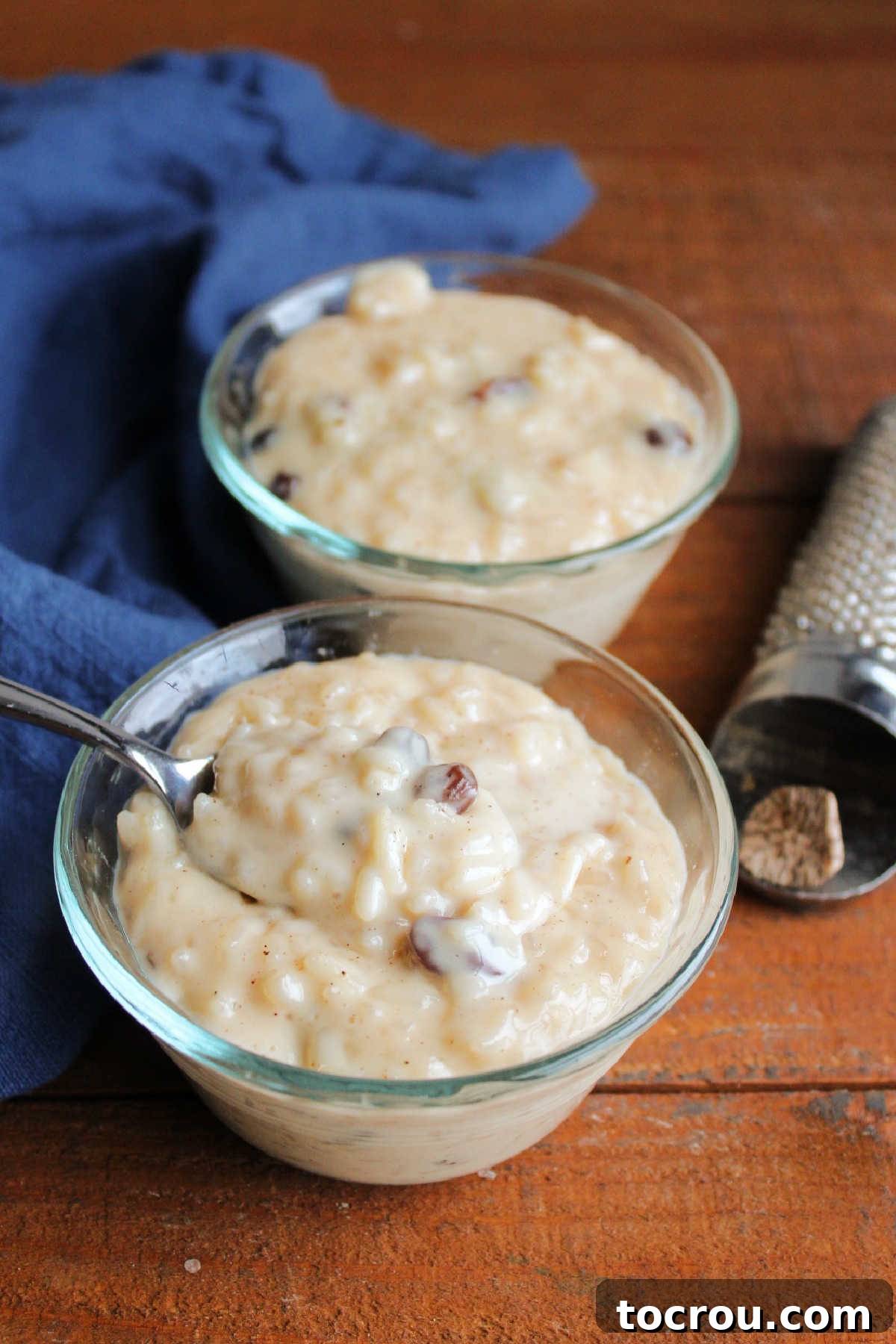 A close-up of a spoon holding a perfect bite of creamy condensed milk rice pudding, speckled with raisins, ready to be enjoyed.