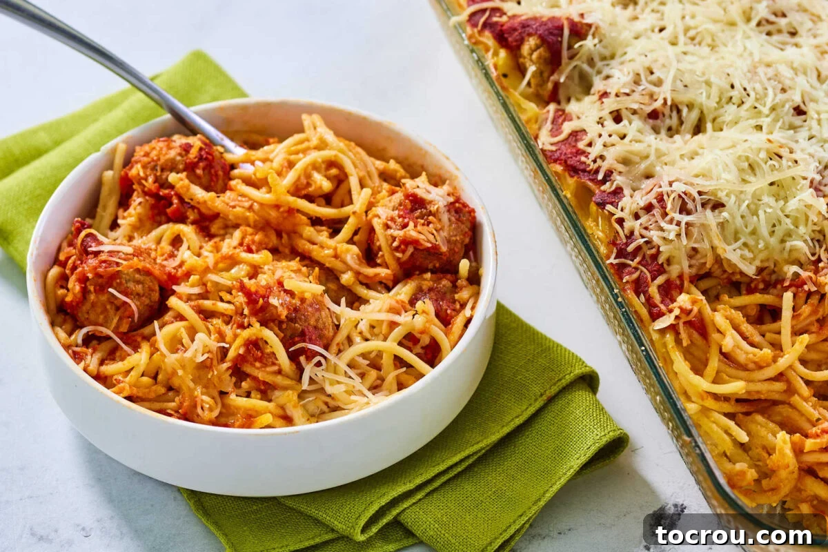 Bowl of cheesy baked spaghetti and meatballs next to casserole dish with more pasta inside.