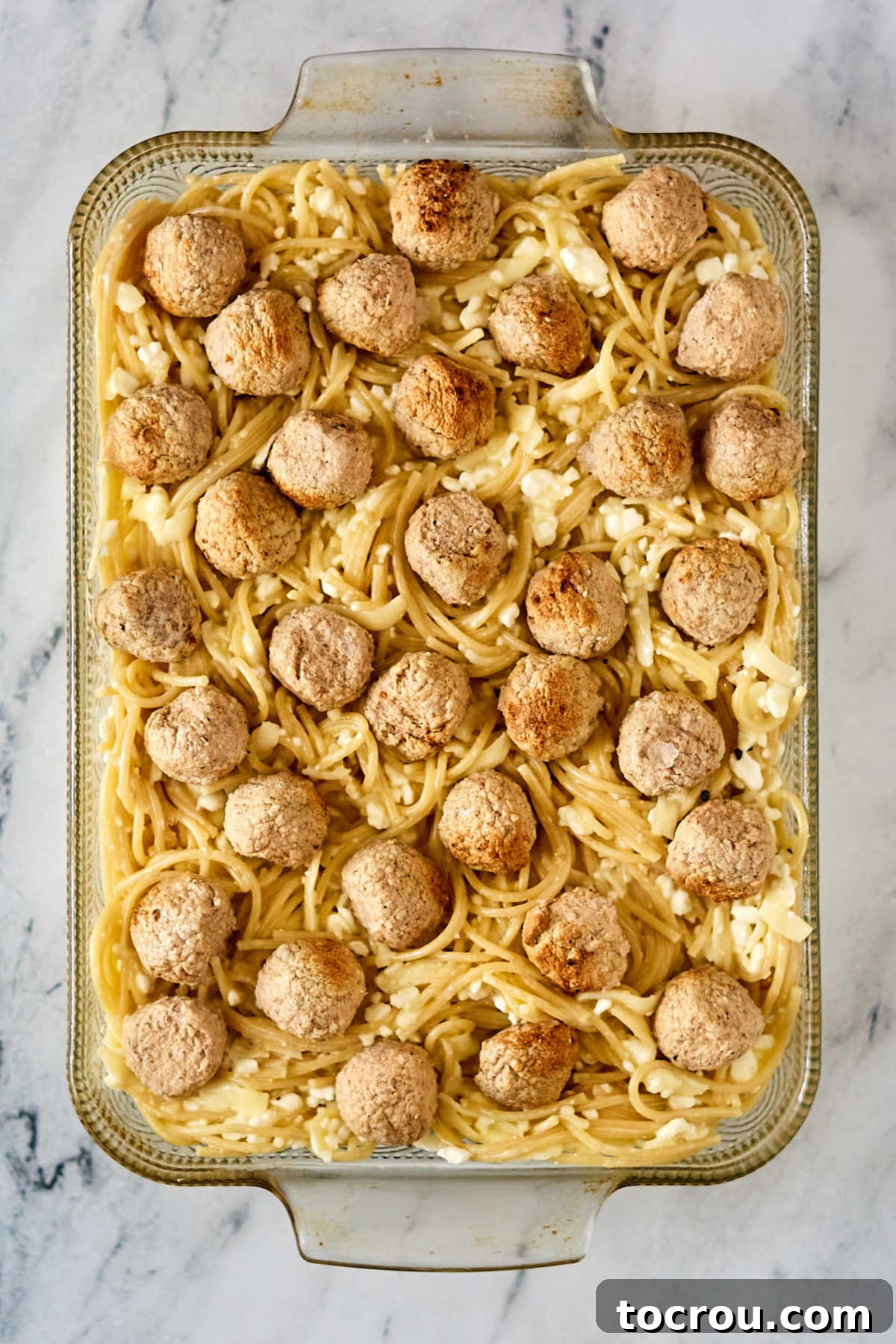 Egg and cheese coated spaghetti in a casserole dish with meatballs scattered over the top.