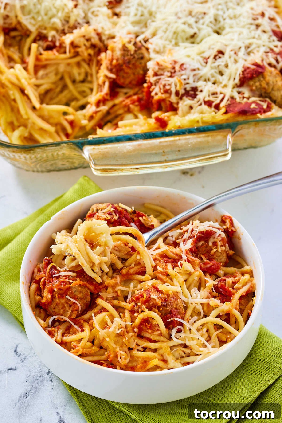 Bowl of baked spaghetti and meatballs next to casserole dish with more inside.