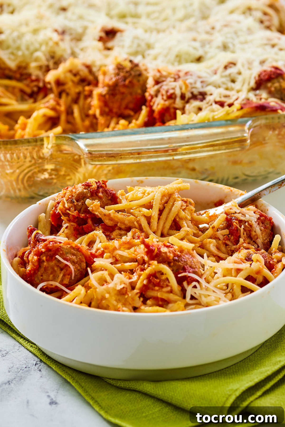 Bowl of cheesy spaghetti and meatball bake with fork, ready to eat.
