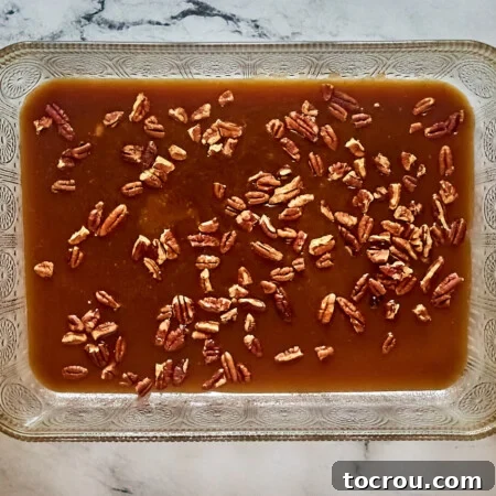 9x13-inch pan with warm caramel mixture and chopped pecans inside.
