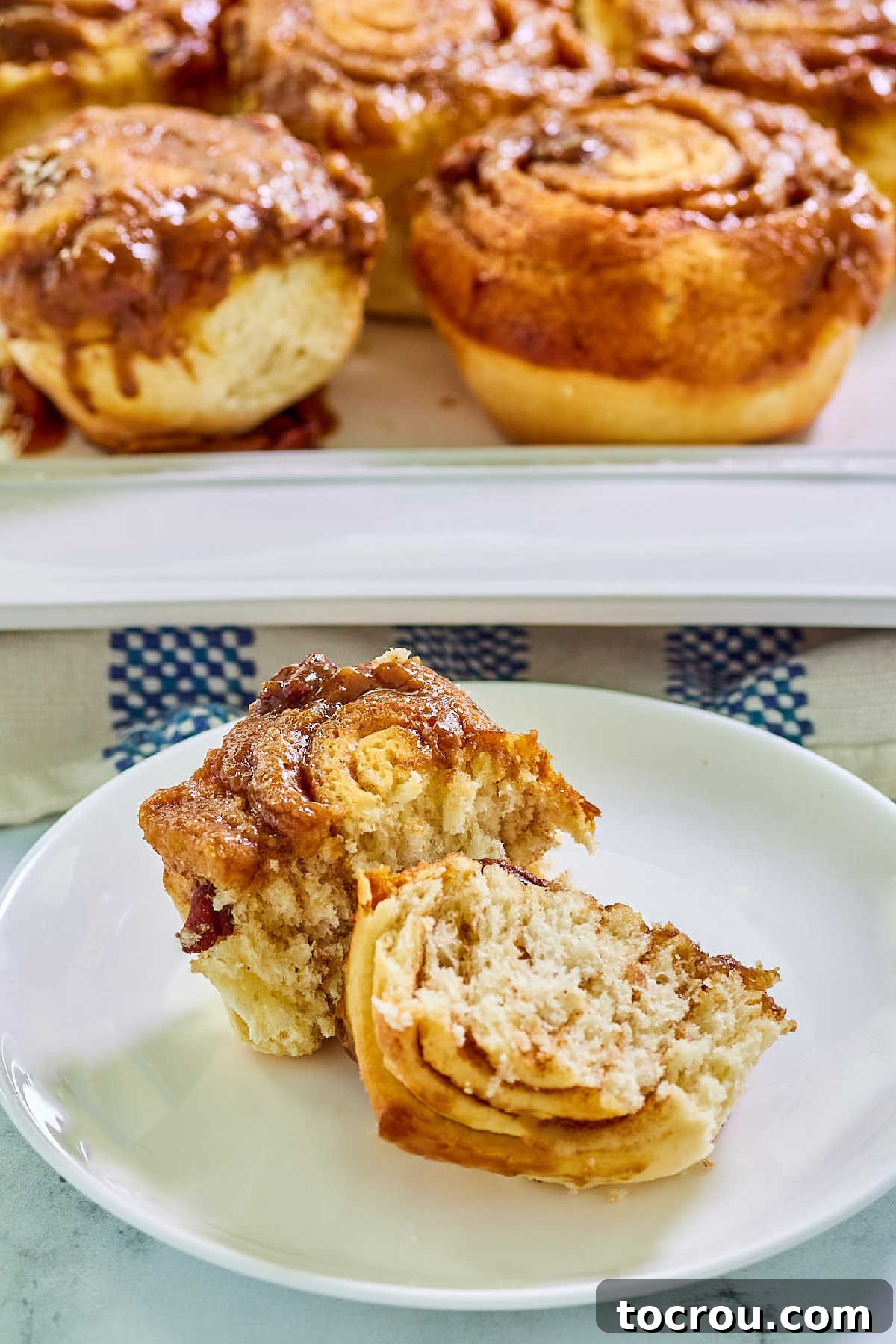 Caramel sticky bun cut in half showing layers of cinnamon between the layers of roll with sticky caramel and pecan topping with remaining rolls in the background. 