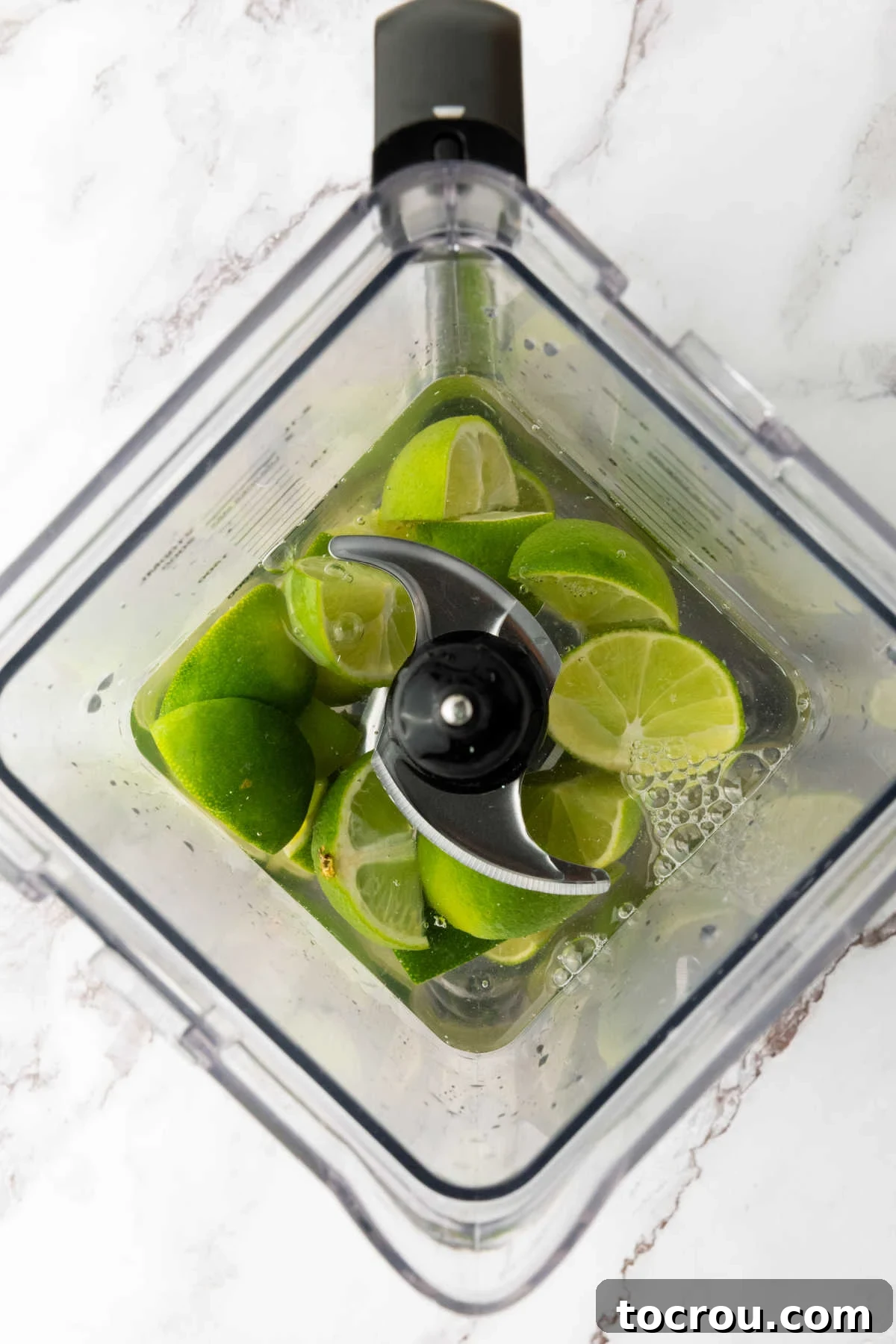 Roughly chopped lime wedges submerged in water inside a blender cup, ready for blending.
