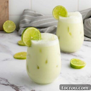 Two glasses filled with creamy limeade, plenty of ice and garnished with a slice of lime, ready to drink.