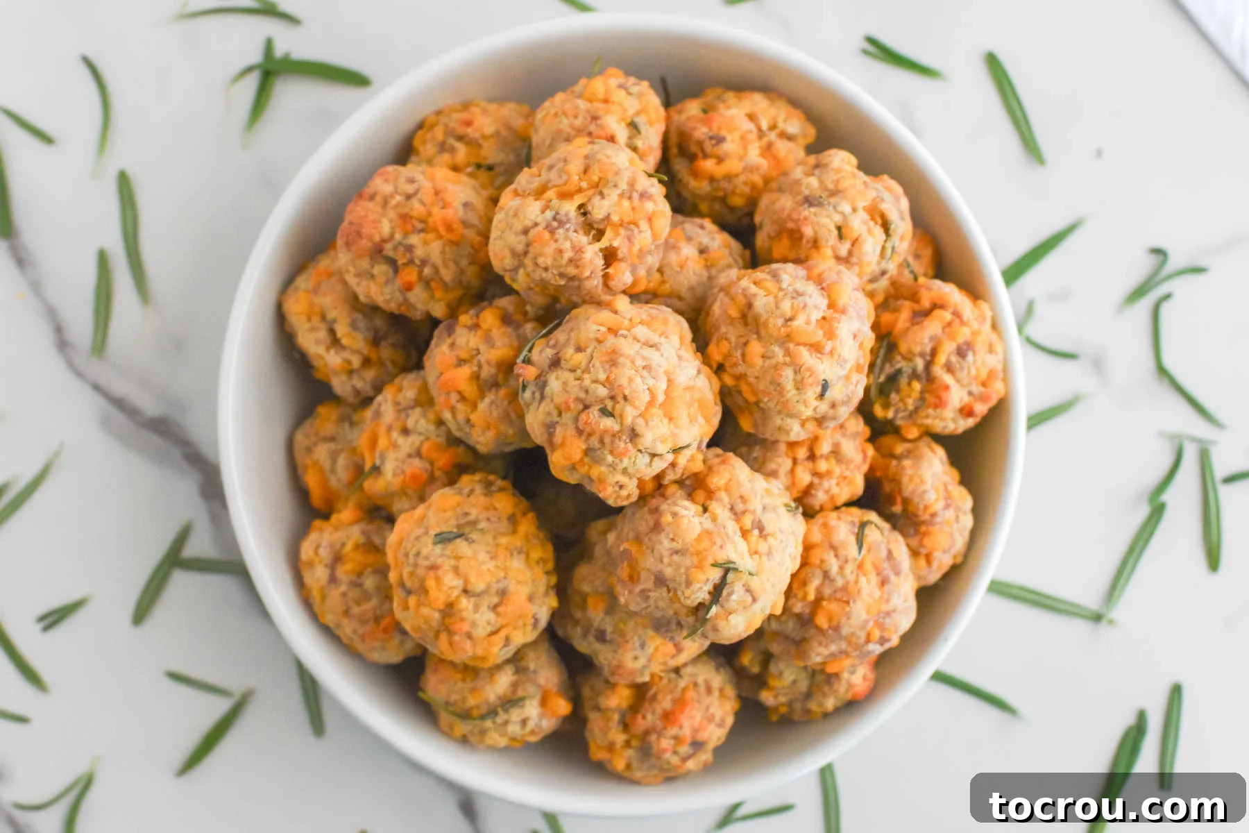 Sausage Cheese Bites 2 Bowl of bisquick sausage balls with cheddar cheese surrounded by bits of rosemary.