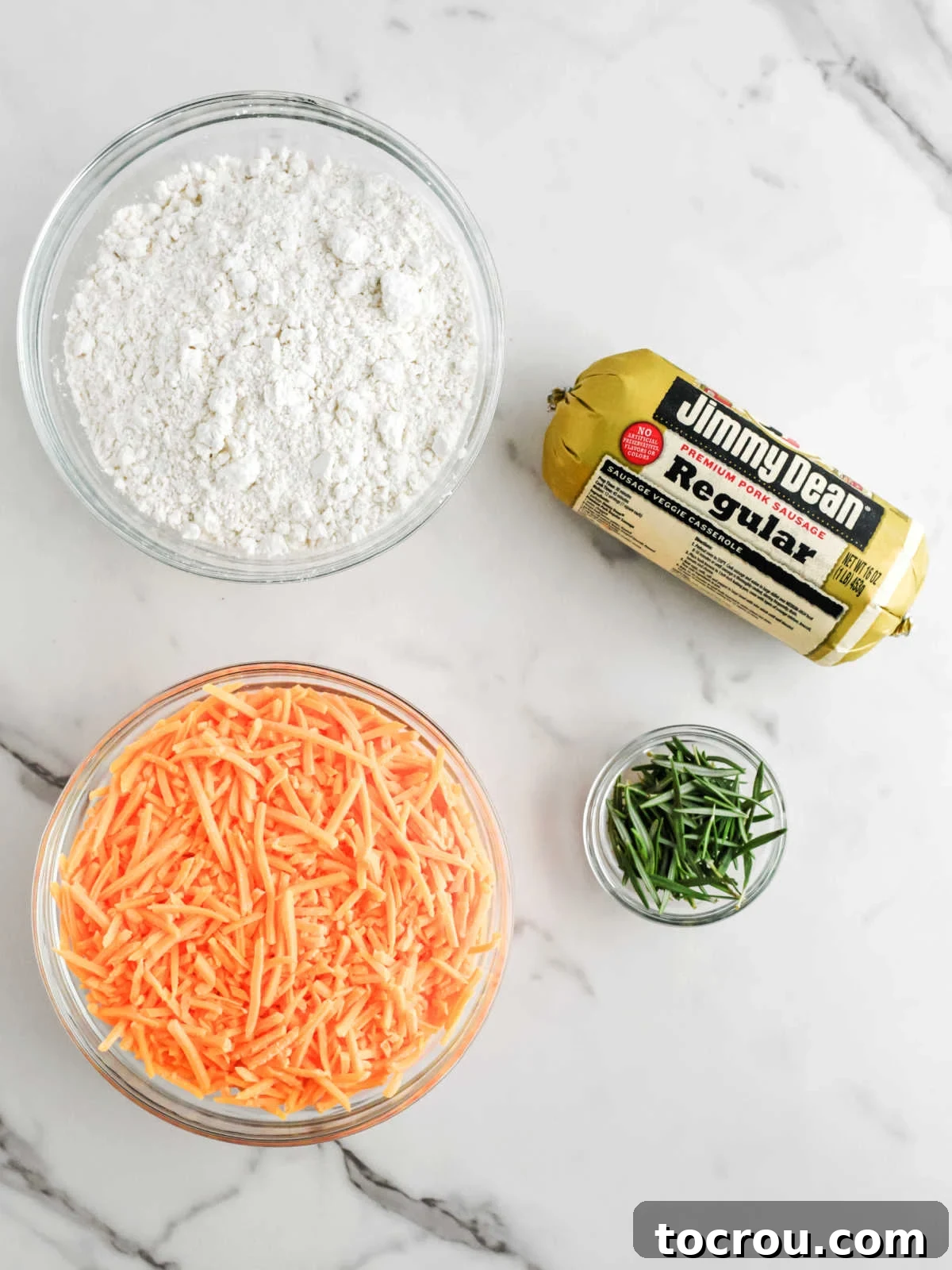 Sausage Cheese Bites 3 Ingredients including a roll of Jimmy Dean sausage, shredded cheddar cheese, fresh rosemary, and Bisquick baking mix.