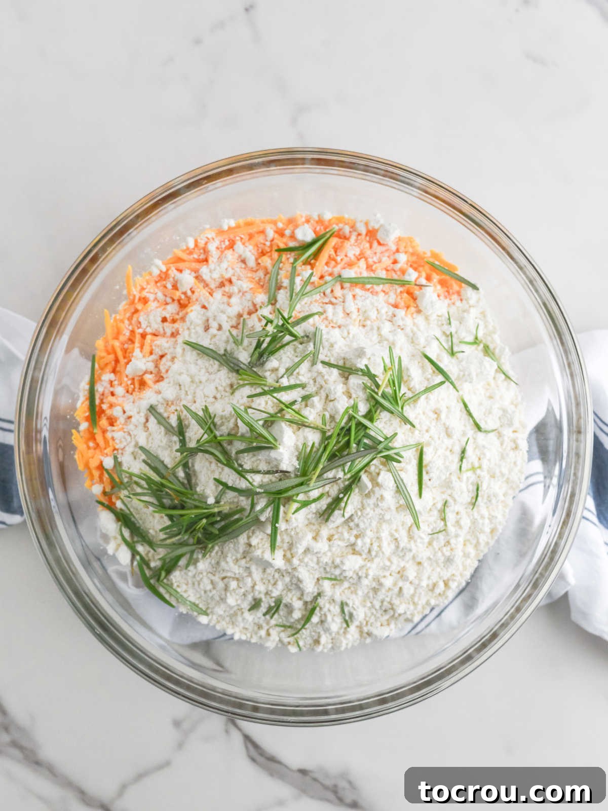 Sausage Cheese Bites 5 Glass mixing bowl filled with raw sausage, bisquick, shredded cheddar cheese and some fresh rosemary.