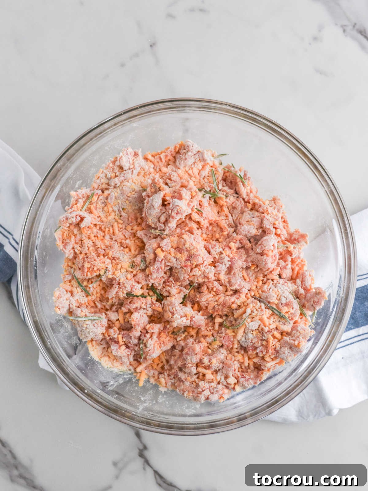 Sausage Cheese Bites 6 Large glass mixing bowl of sausage ball mixture after the cheese, bisquick, and rosemary have been mixed into the sausage.