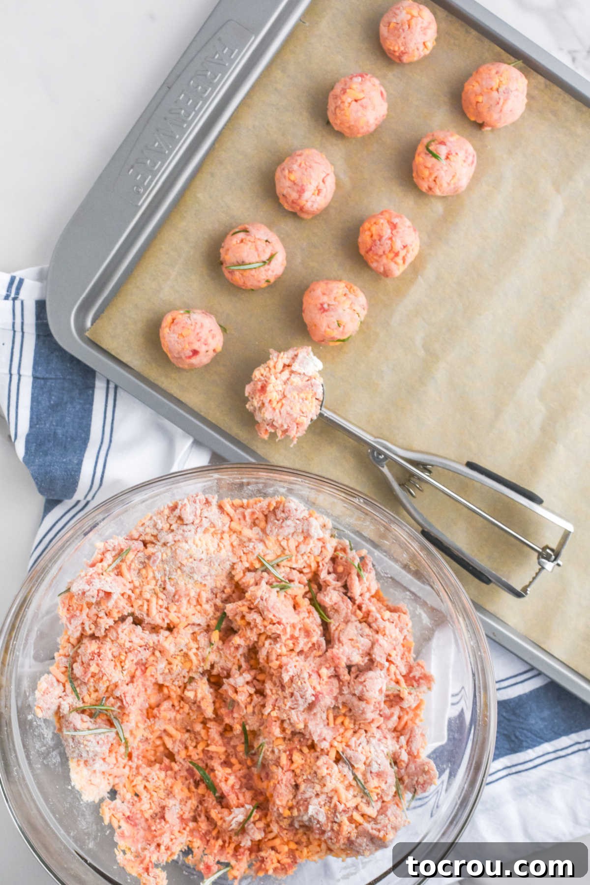 Sausage Cheese Bites 7 Bowl of sausage ball mixture next to parchment lined baking sheet, using a cookie scoop to portion out the meat mixture onto the tray.