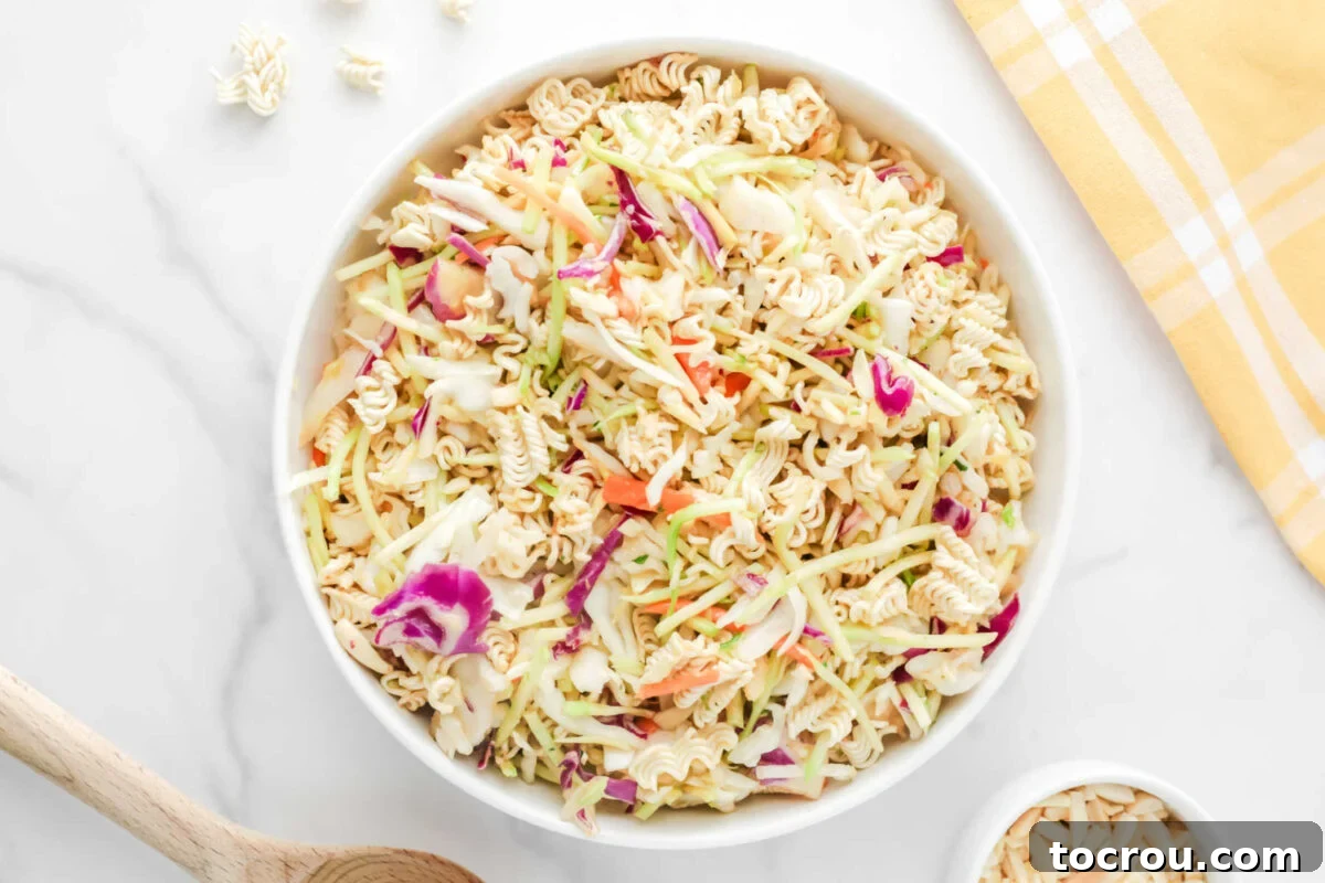 Crunchy Ramen Slaw 2 Large serving bowl filled with a colorful coleslaw mix of shredded green and red cabbage and broccoli, studded with visibly crunchy ramen noodles and delicate slivered almonds, all generously coated in a light, glossy, and flavorful dressing.