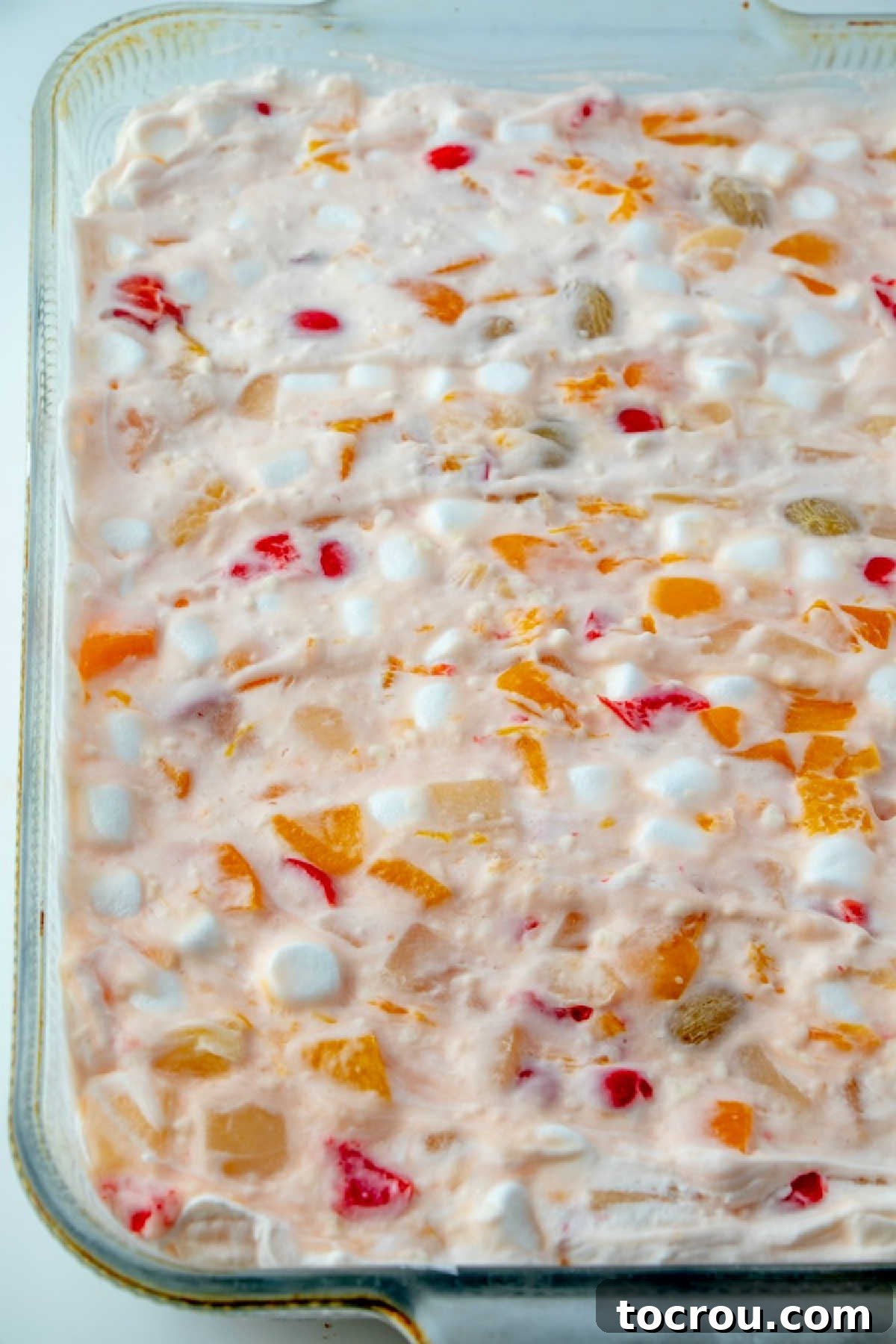 Looking across a glass baking pan filled with frozen fruit salad, revealing a rich tapestry of fruit cocktail bits and fluffy marshmallows frozen together.