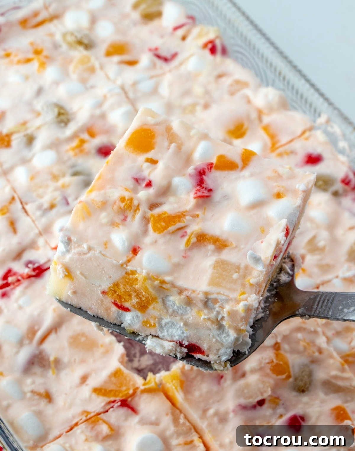 A perfectly square piece of pink frozen fruit salad being gently lifted from the pan, ready to be served and enjoyed.