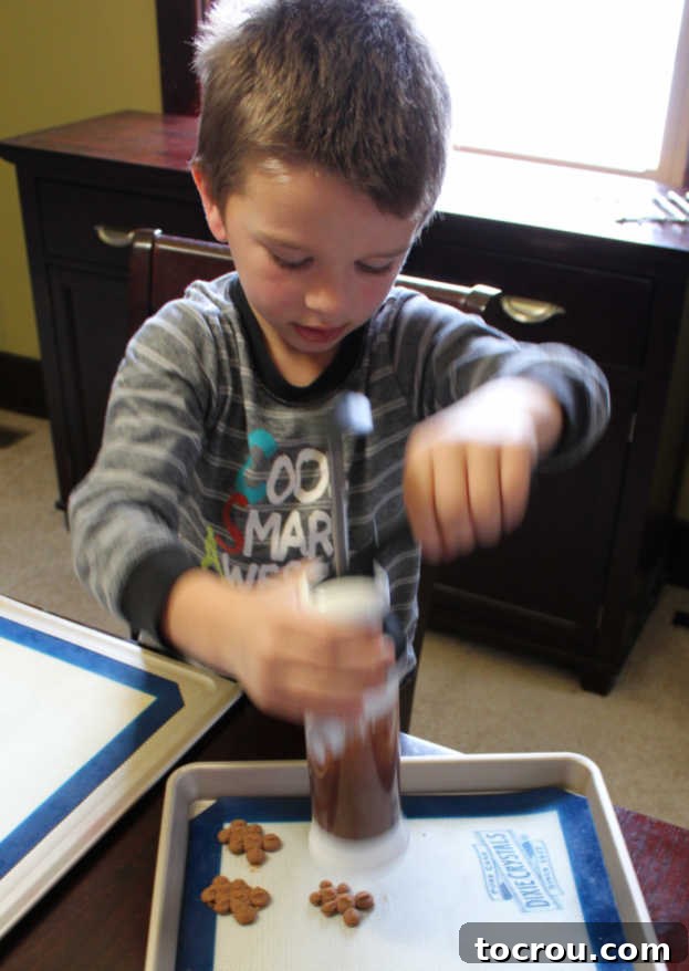 A close-up of a person using a cookie press to form adorable bear and heart-shaped chocolate cookies directly onto a baking sheet.