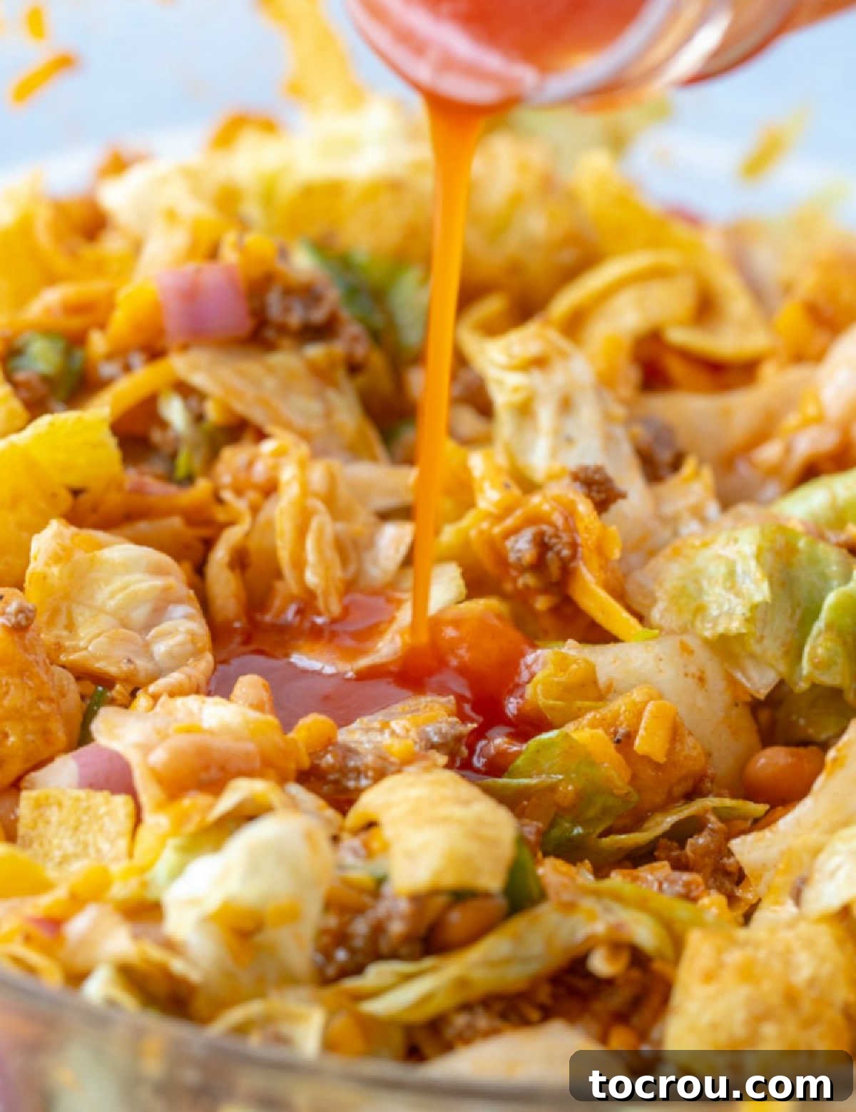 Homemade Catalina Dressing enriches the Frito Taco Salad with its vibrant flavor. Pouring rich, homemade red Catalina salad dressing over a bountiful salad filled with an assortment of fresh ingredients and delightful toppings.