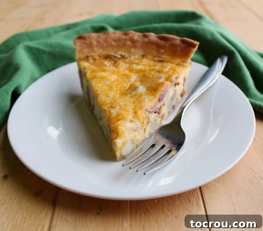 A delectable slice of ham, potato, and cheese quiche, perfectly golden brown, served on a plate with a fork, inviting you to take a bite.
