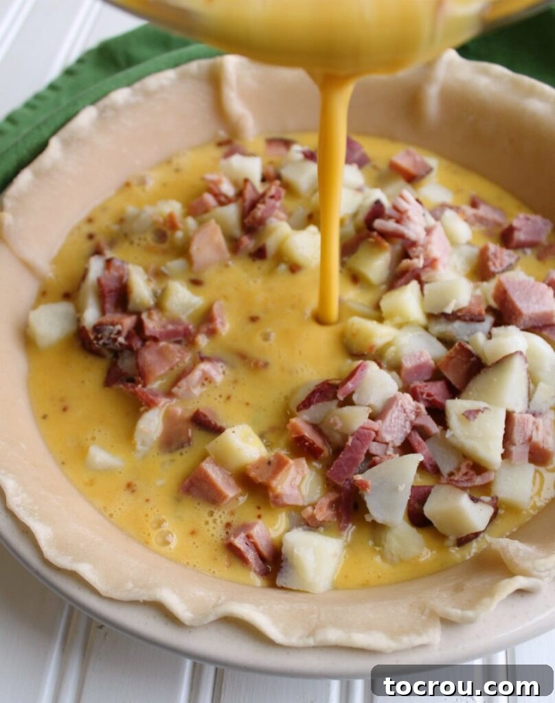 The process of pouring the creamy egg mixture over the ham and potatoes nestled in the pie shell, preparing for baking.