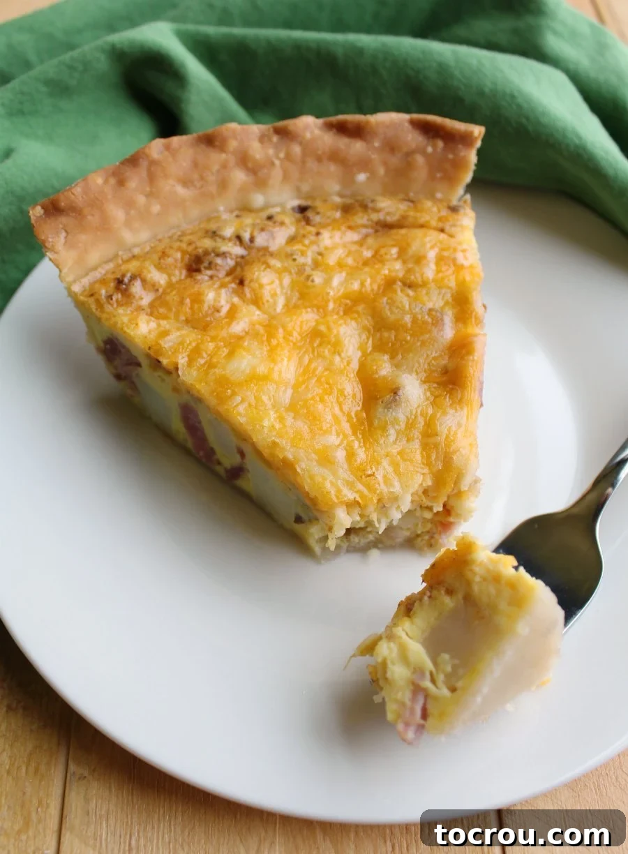 A close-up shot of a slice of ham, potato, and cheese quiche, with a fork holding the first mouth-watering bite, showcasing its golden crust and rich filling.
