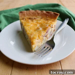 Slice of ham, potato and cheese quiche on plate with fork.