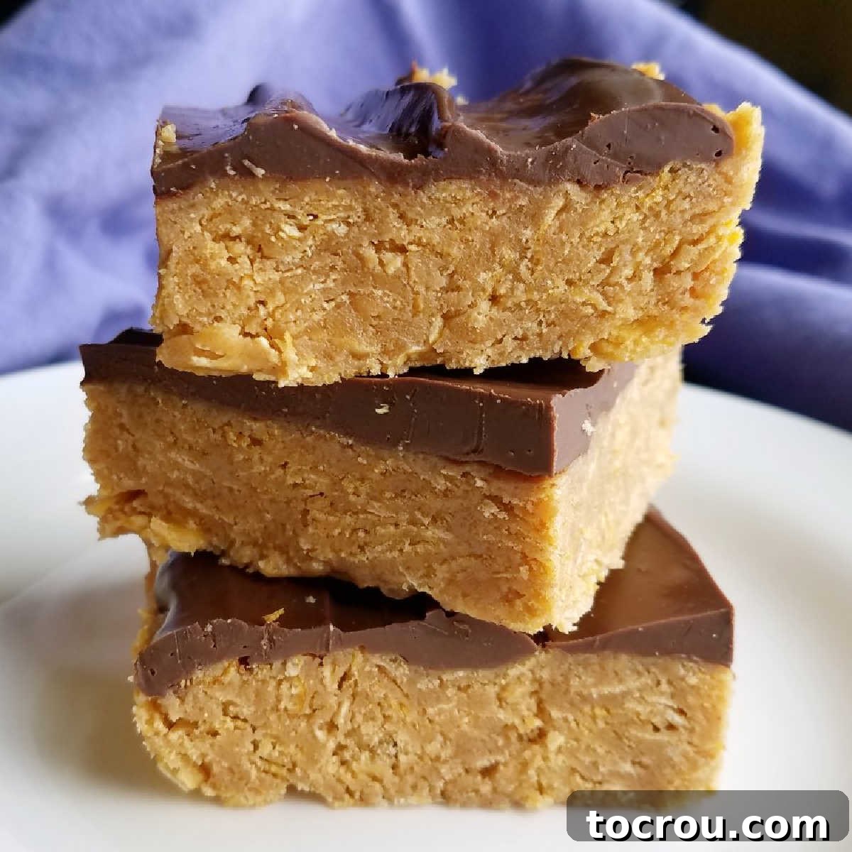 Delicious no-bake chocolate peanut butter cornflake bars ready to be devoured. Stack of perfectly cut peanut butter cornflake bars with a decadent chocolate topping.