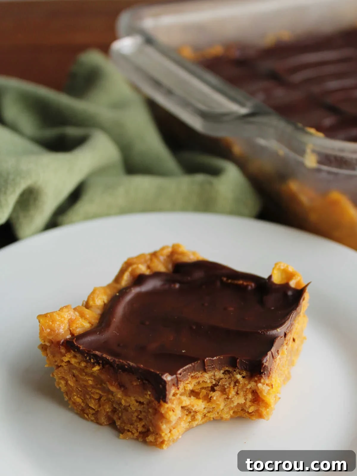 Perfect texture: chewy peanut butter base with crispy cornflakes. A close-up of a peanut butter cornflake bar with a bite missing, revealing its chewy texture and crunchy cereal bits.