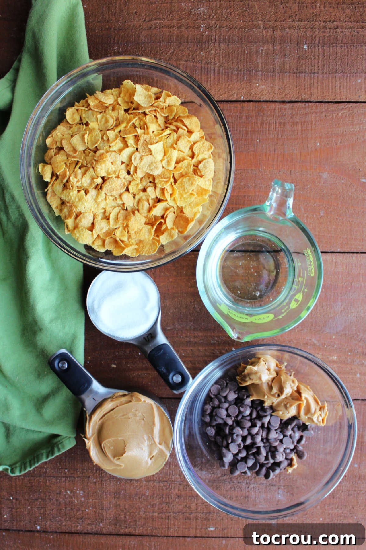 Simple ingredients for an extraordinary no-bake dessert. Key ingredients laid out: cornflakes, creamy peanut butter, granulated sugar, chocolate chips, and light corn syrup.